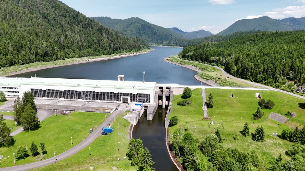 Close aerial view of Čierny Váh hydroelectric power station, showing the dam structure, water channel, and surrounding green landscape in the Slovak mountains
