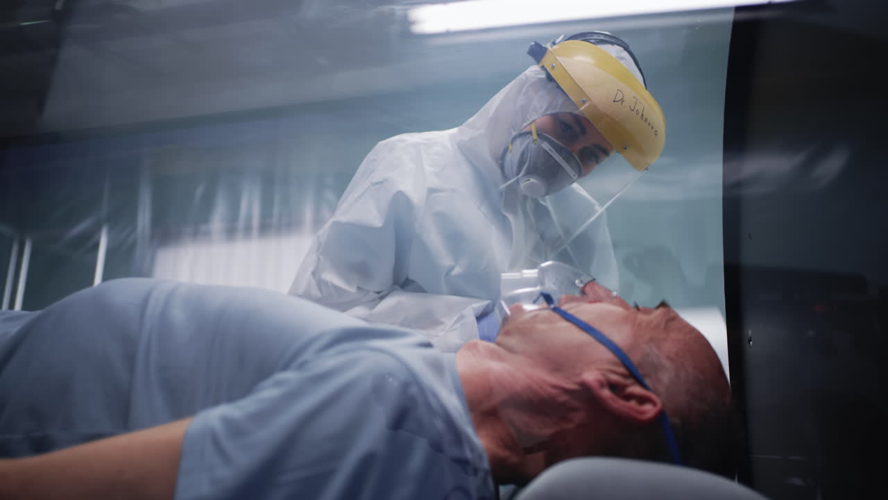 Medical professional in PPE attending to a patient with an oxygen mask