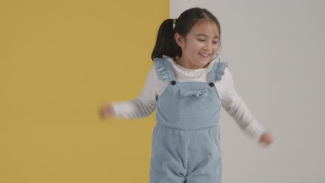 Retrato-De-Estudio-De-Una-Chica-Hiperactiva-Sonriendo-Y-Saltando-Contra-Un-Fondo-Amarillo-Y-Blanco