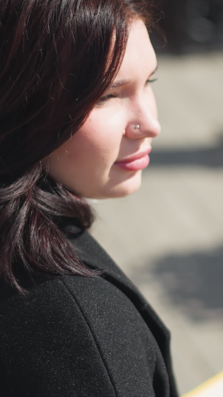 Young woman turns her head with brown hair flowing, nose ring visible, as she looks around in an urban setting , flowers bloom around her as she gracefully moves