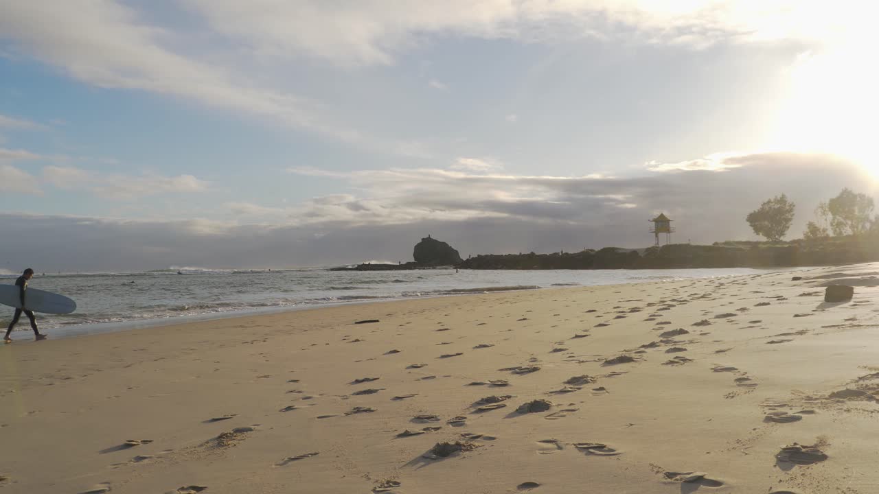 huellas en la arena - surfistas con tabla de surf caminando en la playa durante la puesta de sol después de surfear - playa currumbin - costa dorada, qld, australia