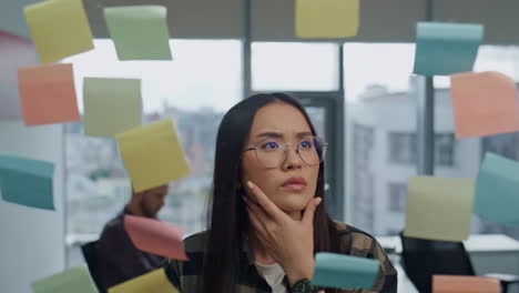 Pondering-manager-writing-sticker-office-close-up.-Asian-woman-planning-project