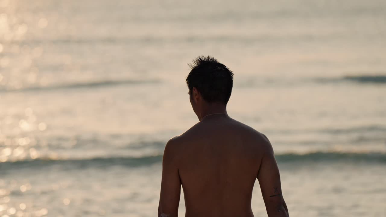 A solitary man stands on a pristine beach in the Maldives, gazing at the vibrant sunset over the calm ocean.