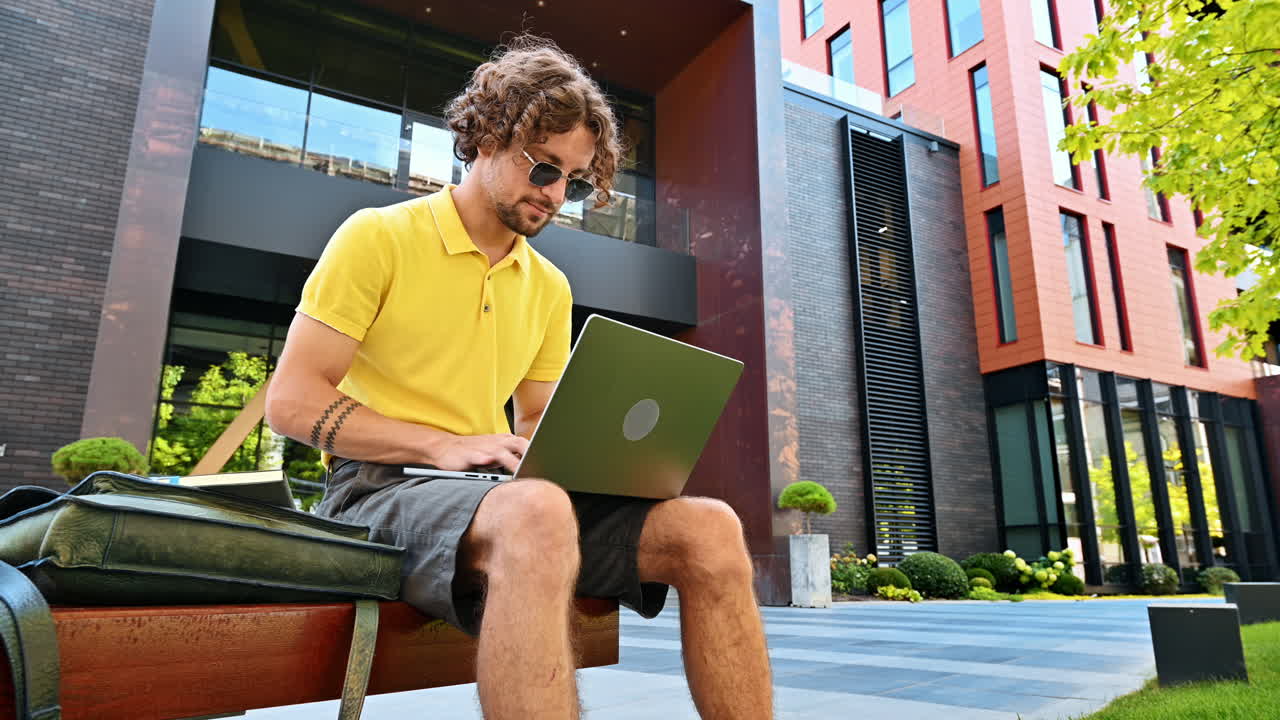 Man in yellow shirt talking standing on a bench and working on a laptop
