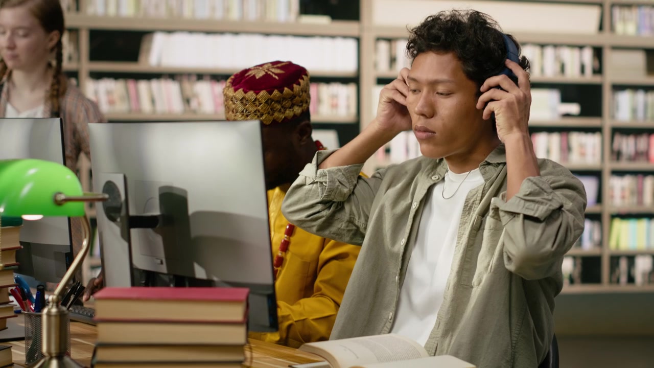 Student adjusting headphones at library study desk with computer