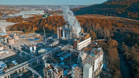 aerial footage moving towards a large industrial chemical plant, showing pipelines, metal structures, cooling towers and chemical storage