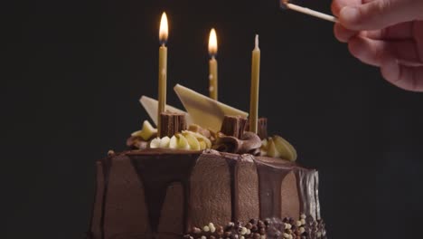 primer plano de estudio de pastel de cumpleaños de chocolate decorado con velas encendidas contra fondo negro