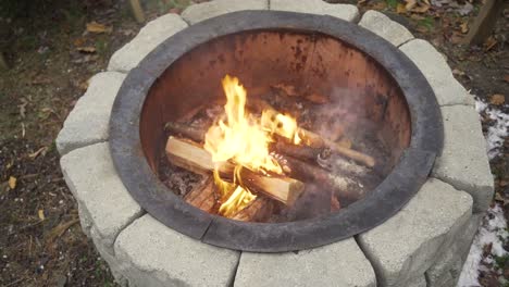 Blick-Von-Oben-Auf-Das-Feuer,-Das-In-Einer-Runden-Steingrube-Mit-Kleinen-Schneemengen-Brennt