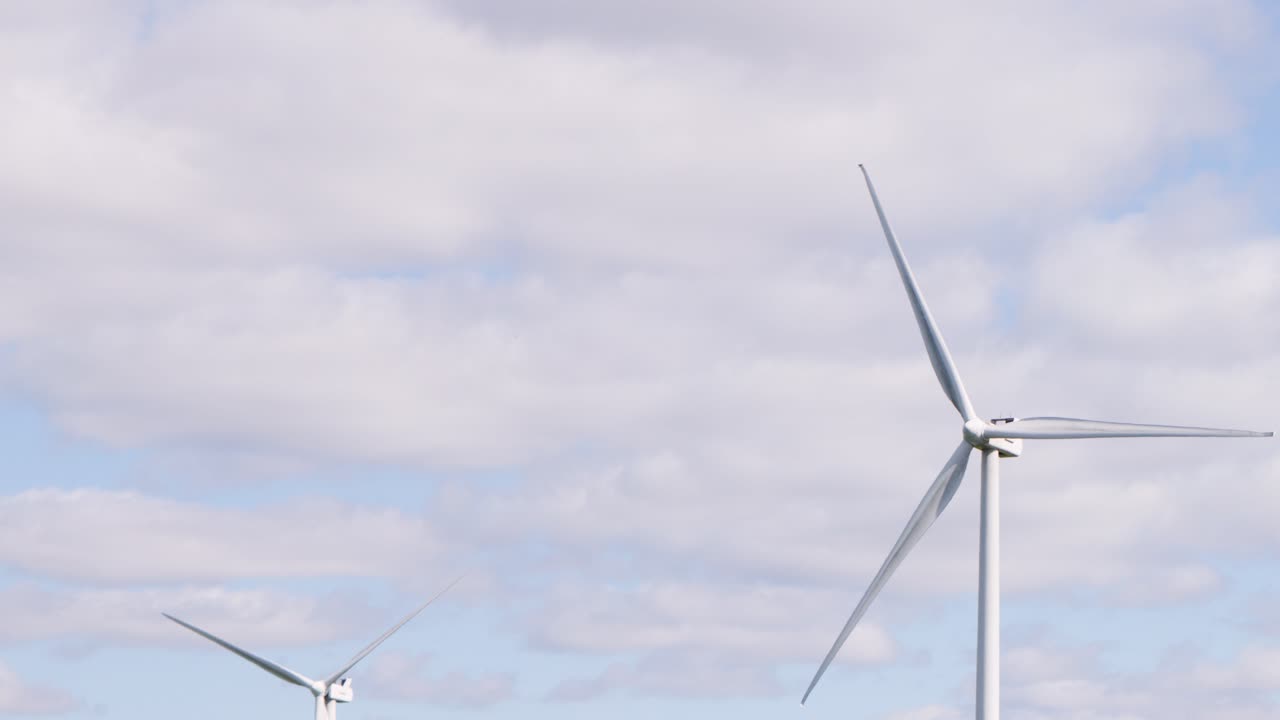 Large wind turbine spins steadily against a partly cloudy sky in the Scottish Highlands. Daylight, wide shot, static camera, clean energy theme