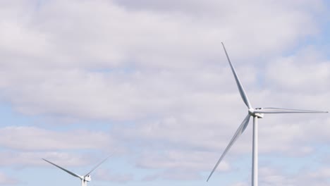 large wind turbine spins steadily against a partly cloudy sky in the scottish highlands. daylight, wide shot, static camera, clean energy theme