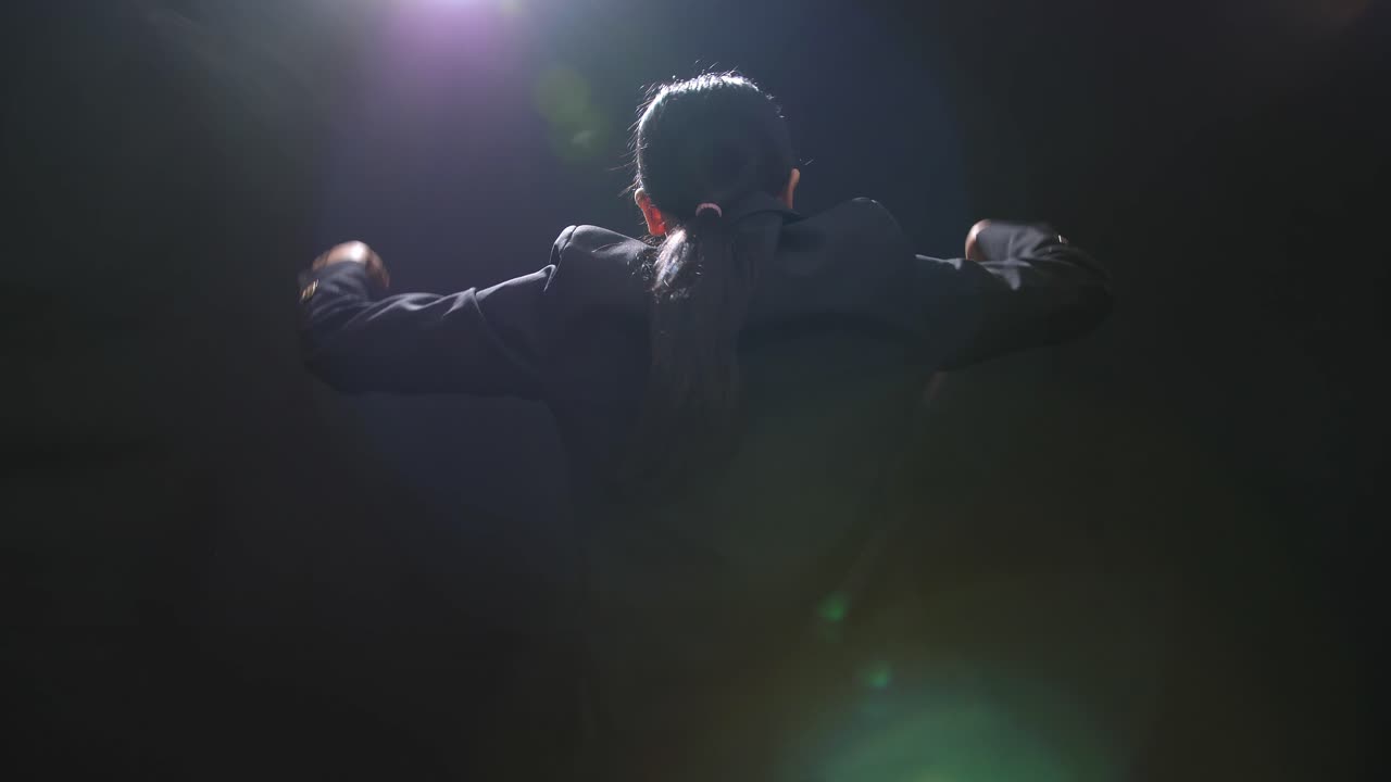 vista trasera de la mujer conductor asiática sosteniendo un bastón y mostrando un gesto rápidamente en el estudio negro con niebla