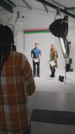 vertical video of actors with scripts in rehearsal shooting movie or video in studio with female director and film crew and watching on monitor 1