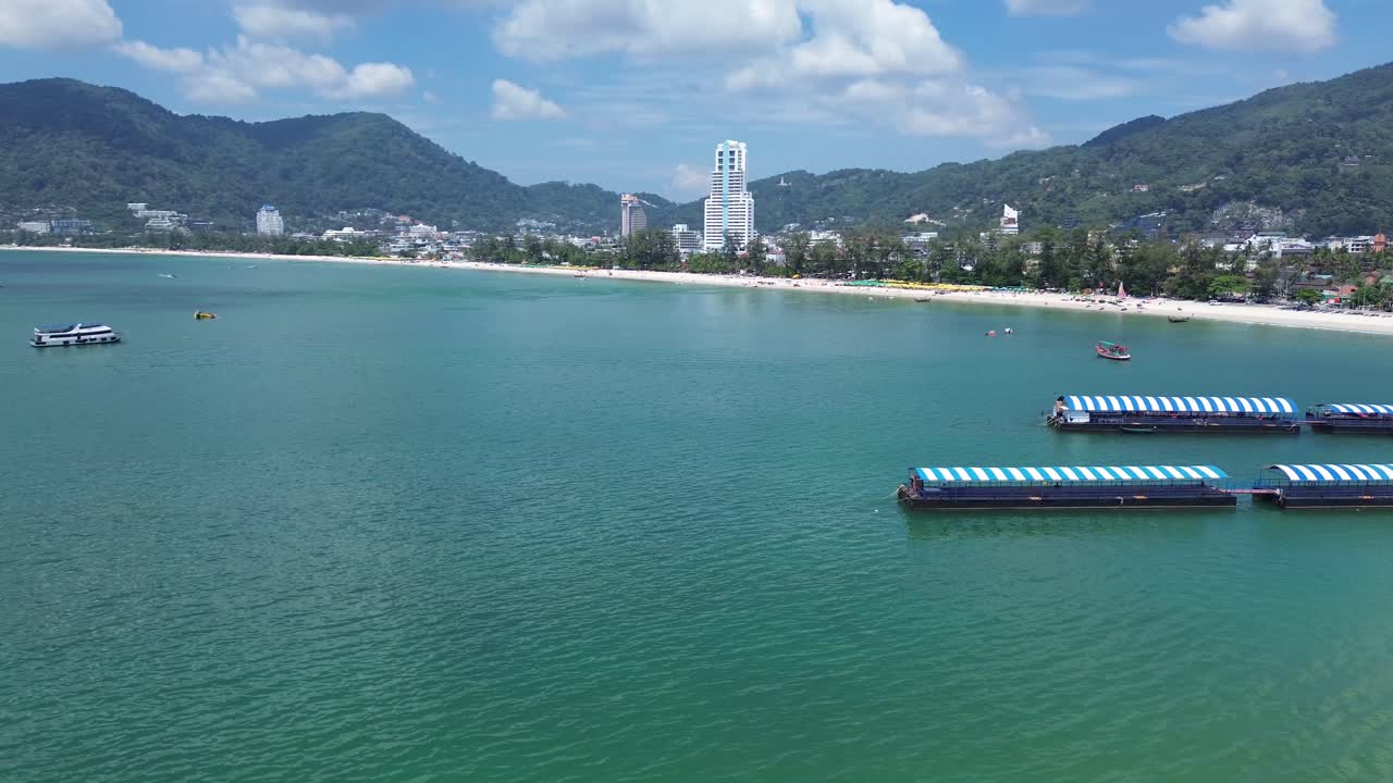 Stunning right-to-left aerial shot capturing Patong’s white sand beach, turquoise waters, and the impressive Phuket skyline under a clear sunny sky.