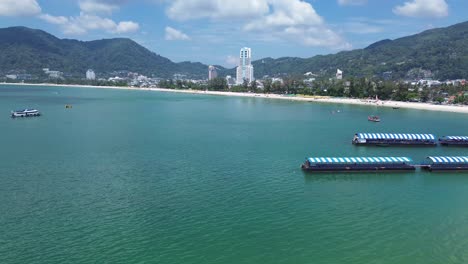 stunning right-to-left aerial shot capturing patong’s white sand beach, turquoise waters, and the impressive phuket skyline under a clear sunny sky.