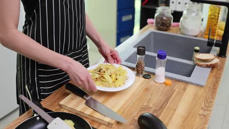 person holding a plate of scrambled eggs and potatoes in a kitchen
