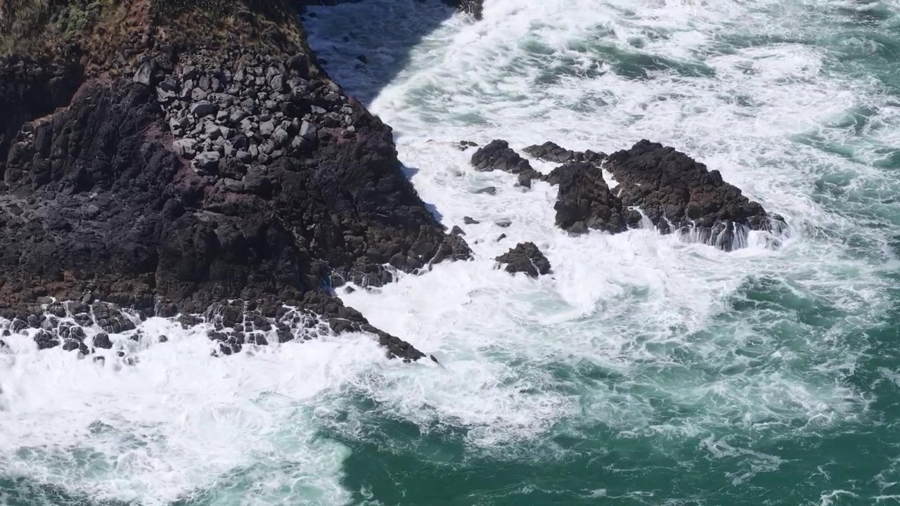 De puissantes vagues océaniques s'écrasant contre des roches côtières volcaniques, sur l'Île du Nord de la Nouvelle-Zélande, offrant une vue spectaculaire sur la nature et le littoral.