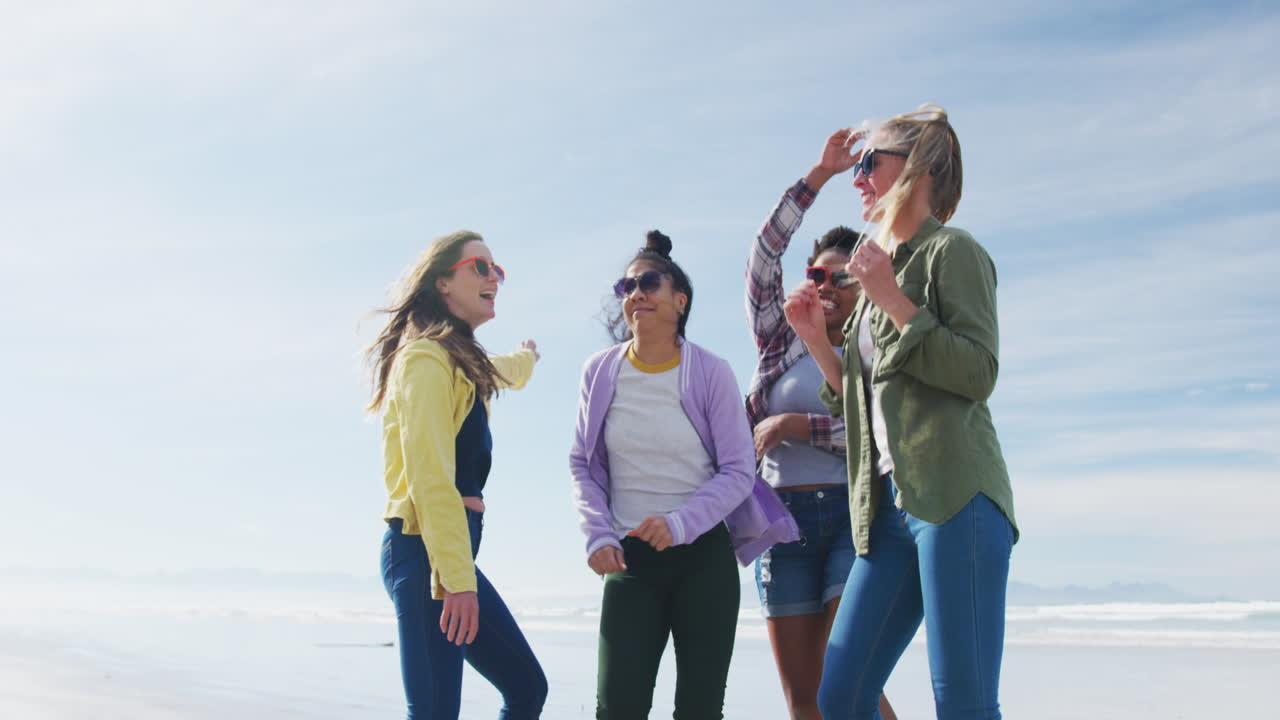 다양한 여성 친구들의 행복한 그룹이 해변에서 재미있고, 춤추고, 미소 짓고 있습니다.