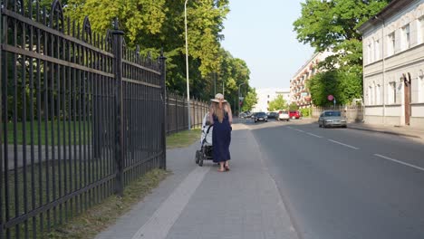 elegant caucasian woman pushing baby stroller in street near park, latvia