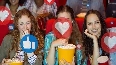 Animation-of-media-icons-over-smiling-caucasian-female-friends-eating-popcorn-in-cinema
