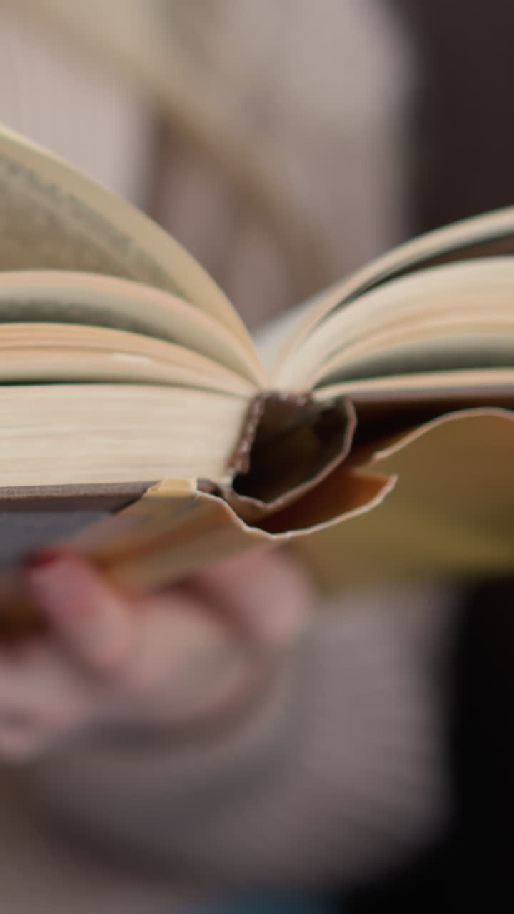 Primo piano di una mano che sfoglia delicatamente una pagina di un libro, mostrando il processo di voltare pagina, con le pagine aperte del libro e il movimento del dito catturati su uno sfondo soffuso.