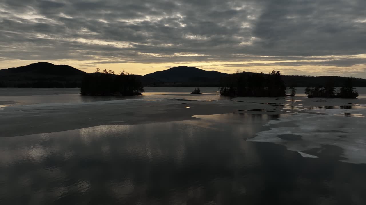 Auringonlasku tyynen jäätyneen järven yllä – talvinen ilmakuva