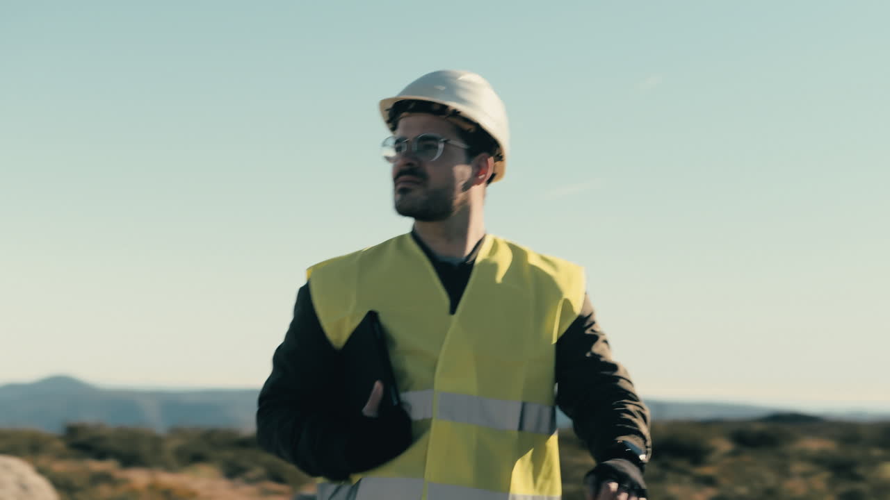 un experto de casco blanco examina las turbinas eólicas en un día soleado, caminando por el campo de los generadores de energía renovable, lo que representa el compromiso con un futuro sostenible