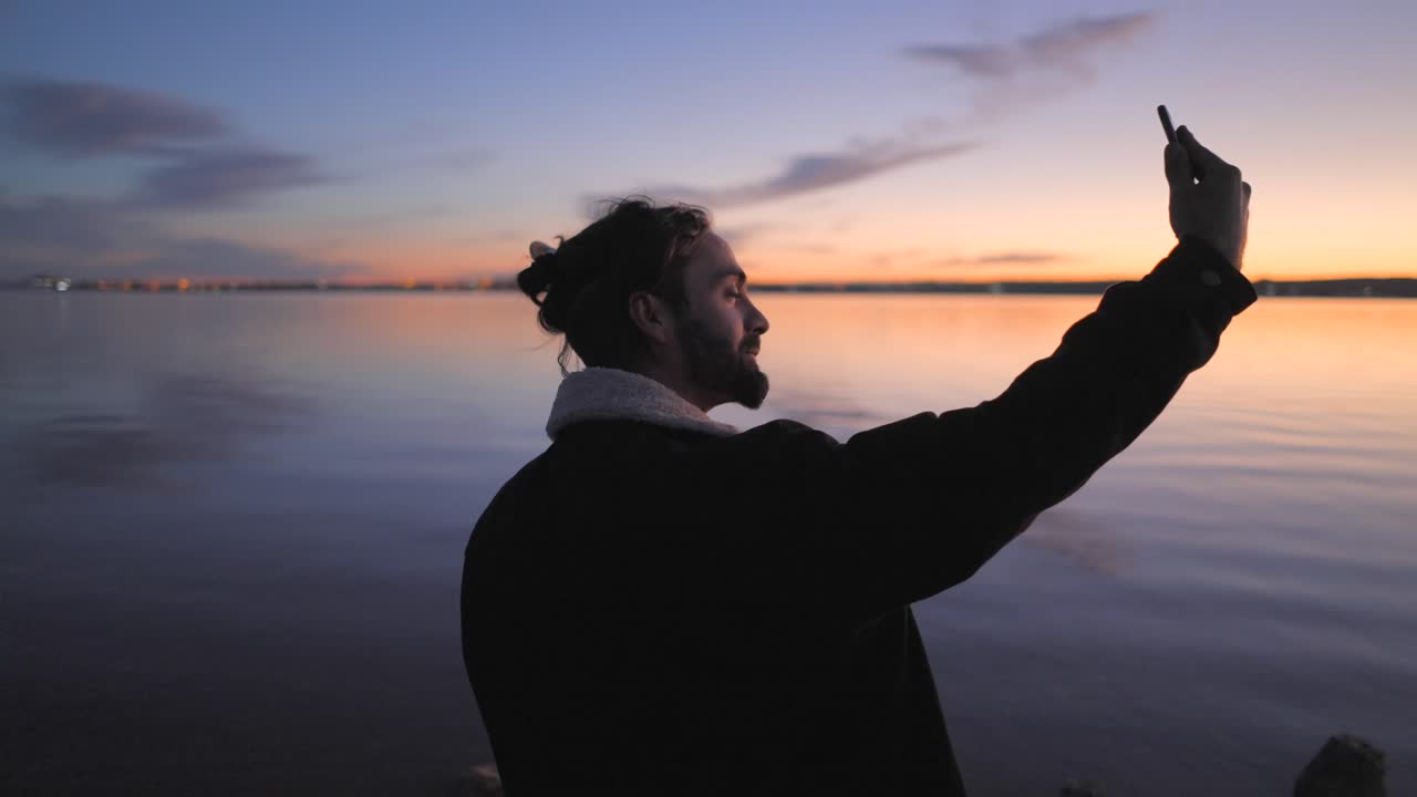 Man taking a selfie with a guitar at sunset by the river