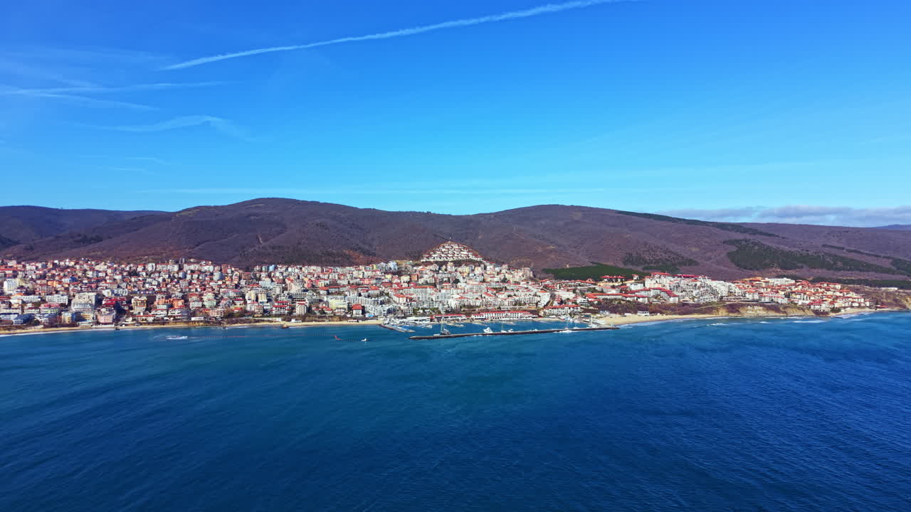 Cittadina costiera sul mare con edifici sulla riva e montagne sullo sfondo durante una giornata di sole