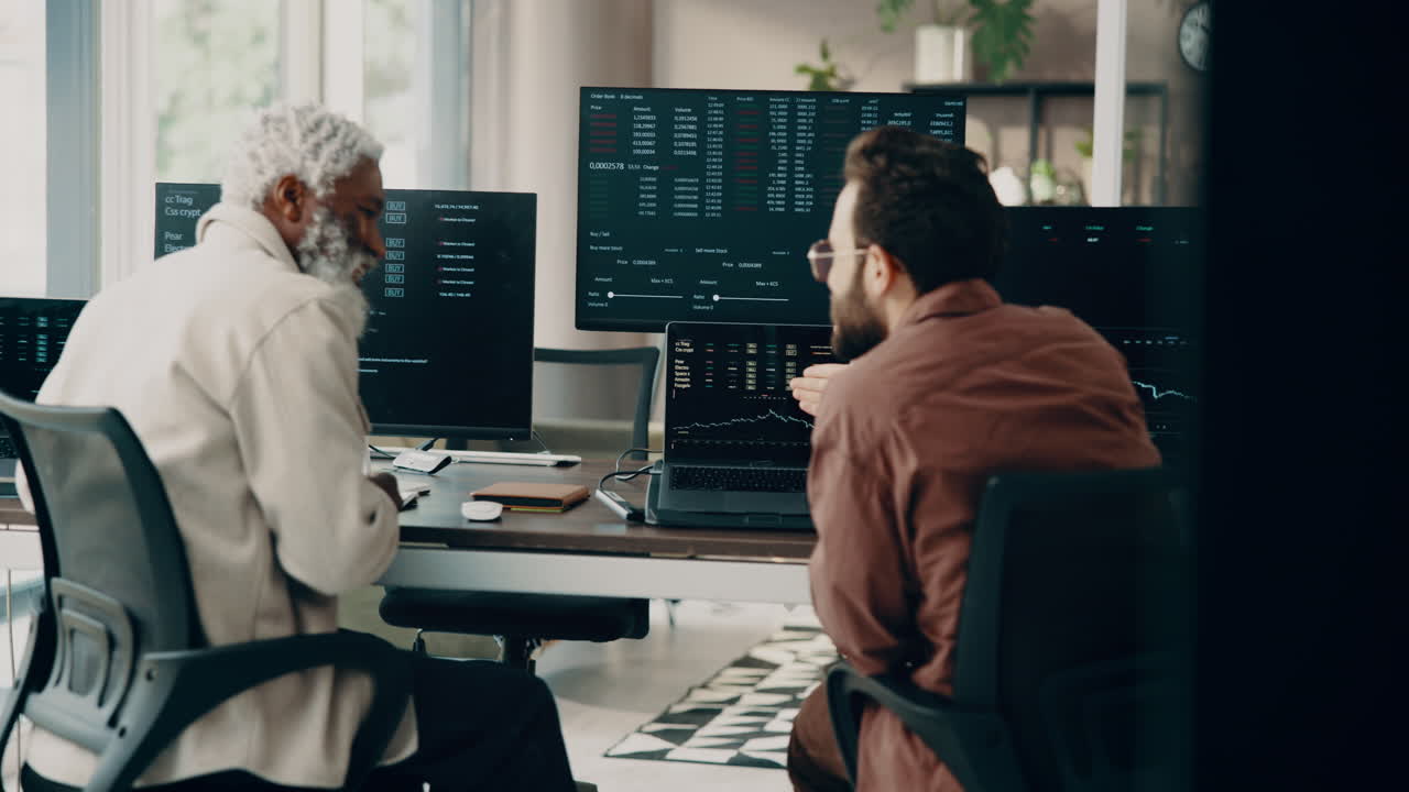 Two men working in an office analyzing stock market data on computers
