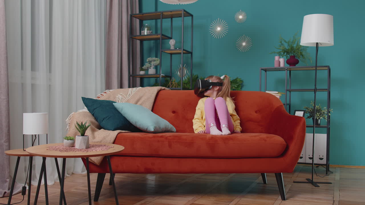 niña pequeña sentada en el sofá de su casa usando una aplicación de casco de realidad virtual para jugar un juego de simulación