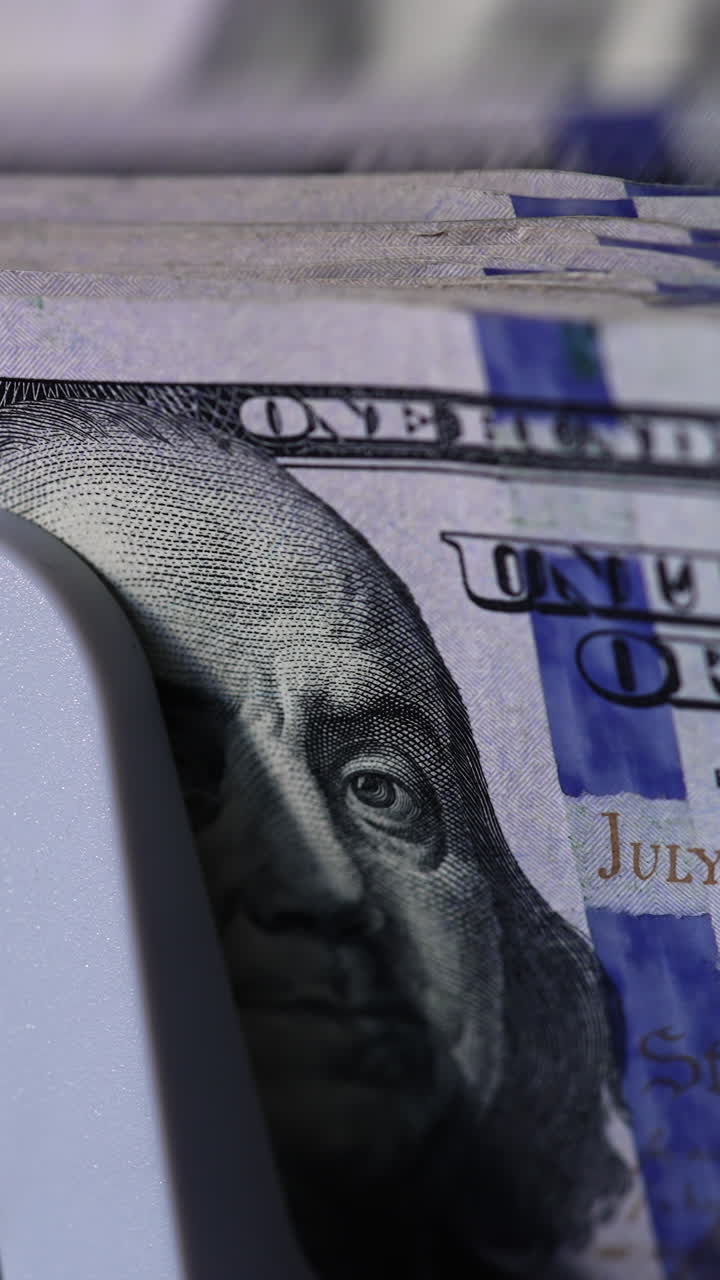 Benjamin Franklin portrait on the dollar bills. Cash counting machine counts American currency bills. Close up. Vertical video