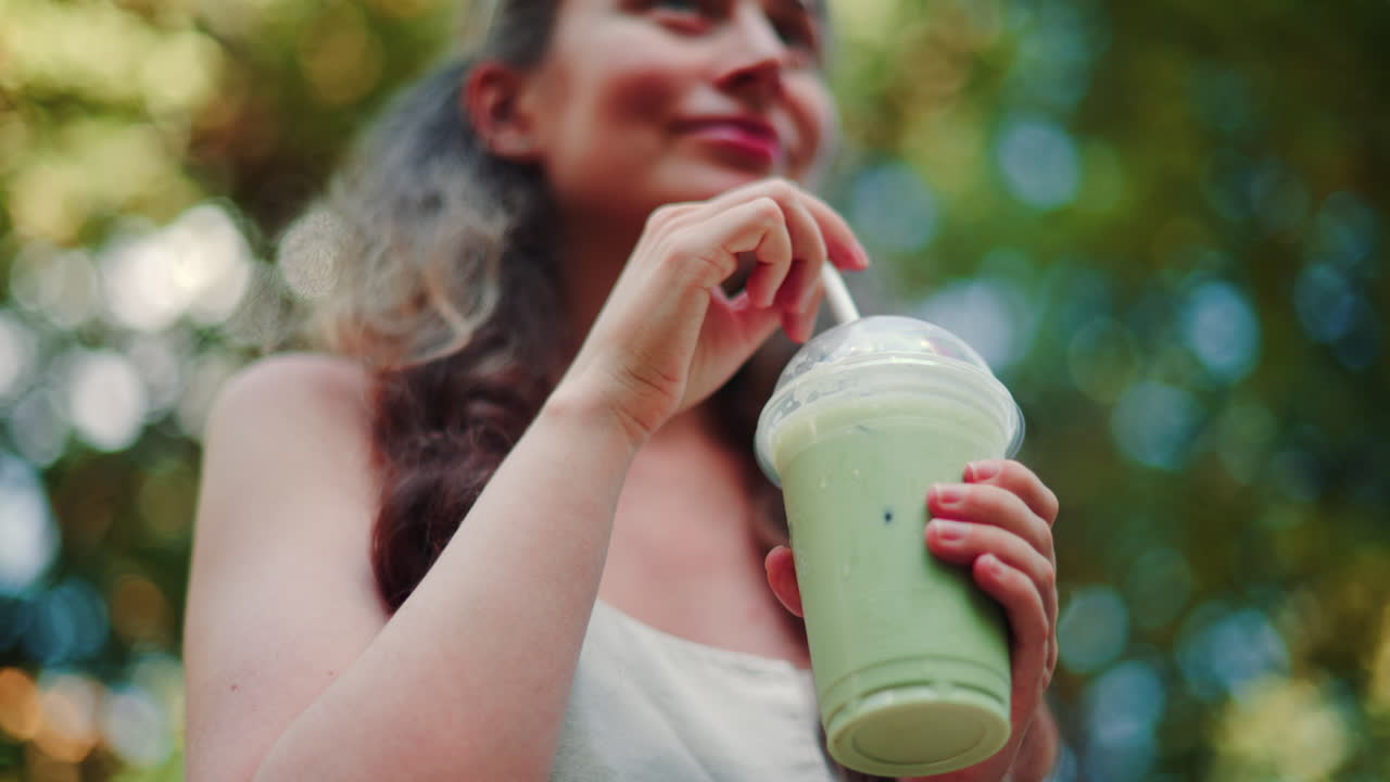 Close up of woman's hand holding an iced matcha latte outdoors