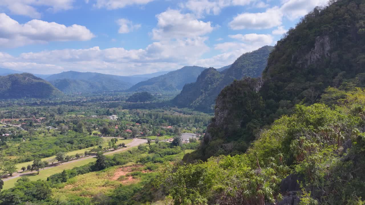 Câmera de drone percorre montanhas verdejantes e formações rochosas de calcário sob o céu azul