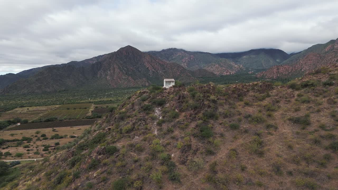 vista aérea de la cima de la montaña en cafayate con una casa religiosa y una impresionante vista del valle y la agricultura y más colinas en el horizonte