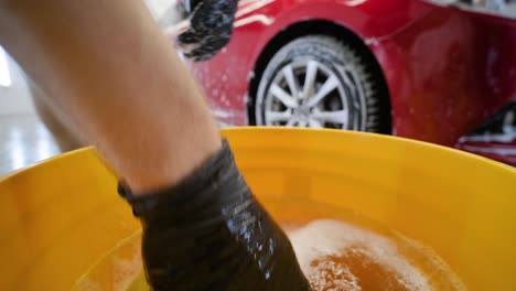 man worker washing red car on a car wash with yellow washcloth.