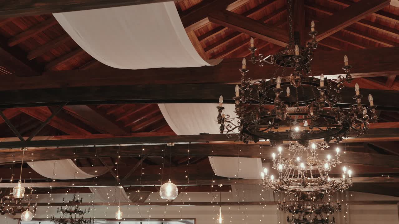 Warmly lit chandeliers and hanging fabric decorating wooden ceiling
