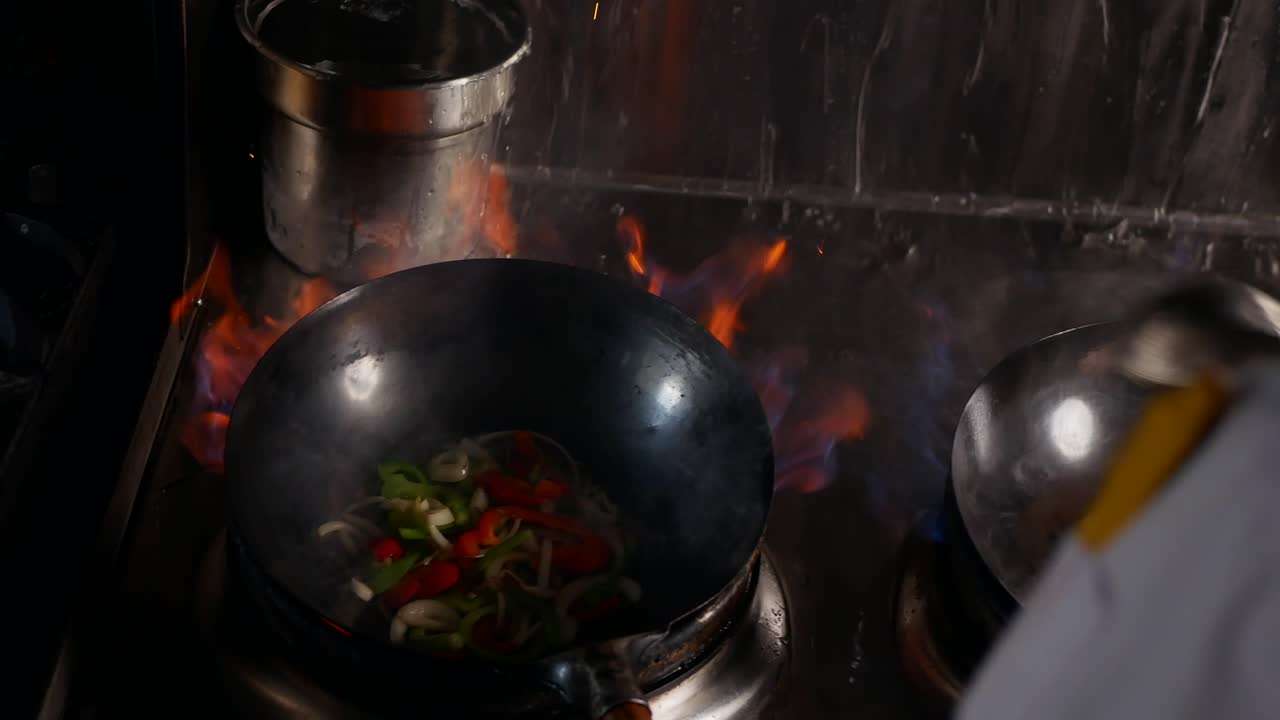Chef thailandese cucina contemporaneamente in tre wok mentre salta le verdure in padella con fiamme