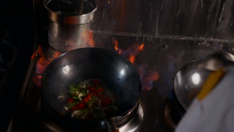 thai chef cooks in three woks simultaneously while stir frying veggies with flames.