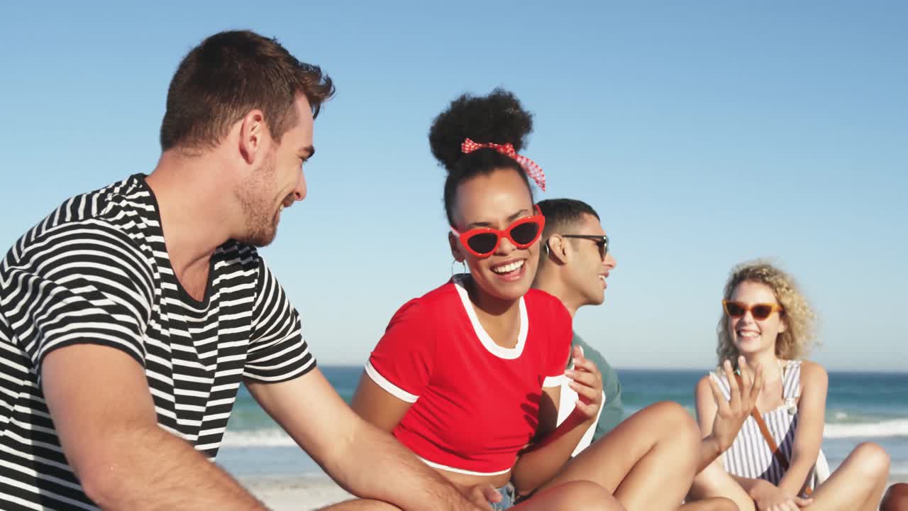 jóvenes amigos adultos sentados en una playa hablando 4k