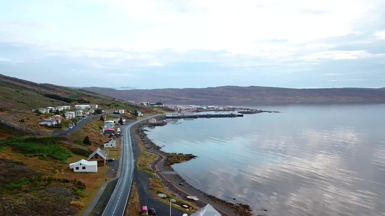 유럽 아이슬란드의 작은 바다 해안 마을을 보여주는 공중 트럭 샷, 아름다운 물 반사, 구름이 있는 밝은 하늘