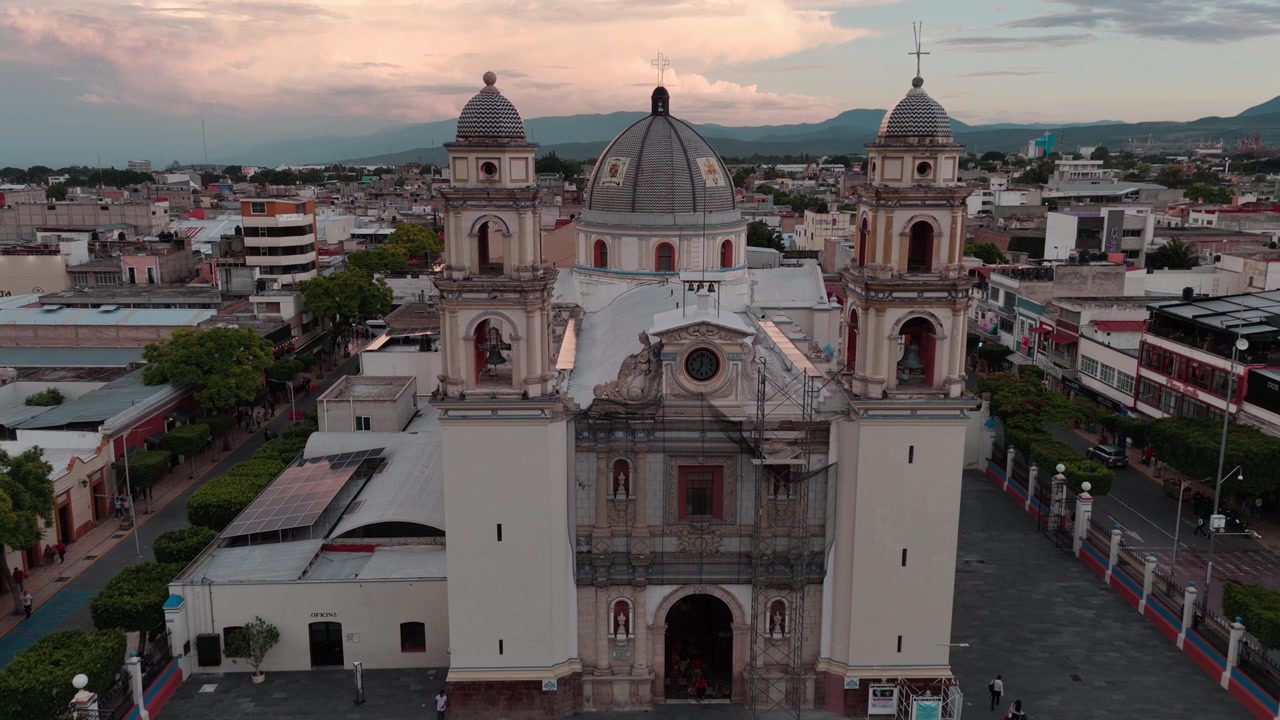 Ripresa aerea con drone di una cattedrale storica con due campanili gemelli e una cupola centrale, che domina il centro città circostante sotto un cielo al tramonto colorato in Messico.