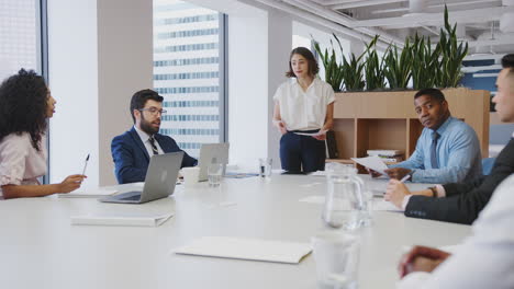 Geschäftsfrau-Hält-Präsentation-Vor-Kollegen,-Die-Im-Modernen-Büro-Am-Tisch-Sitzen