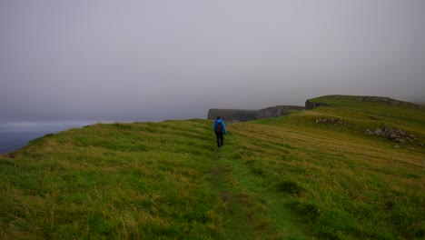 male hiker walk along grassy hill on mykines and turns back calling for someone on a cloudy day, faroe islands