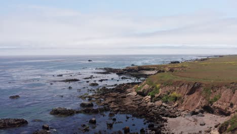 Low-aerial-shot-flying-over-the-rocky-coastline-towards-a-beached-shipwreck-in-Cayucos,-California