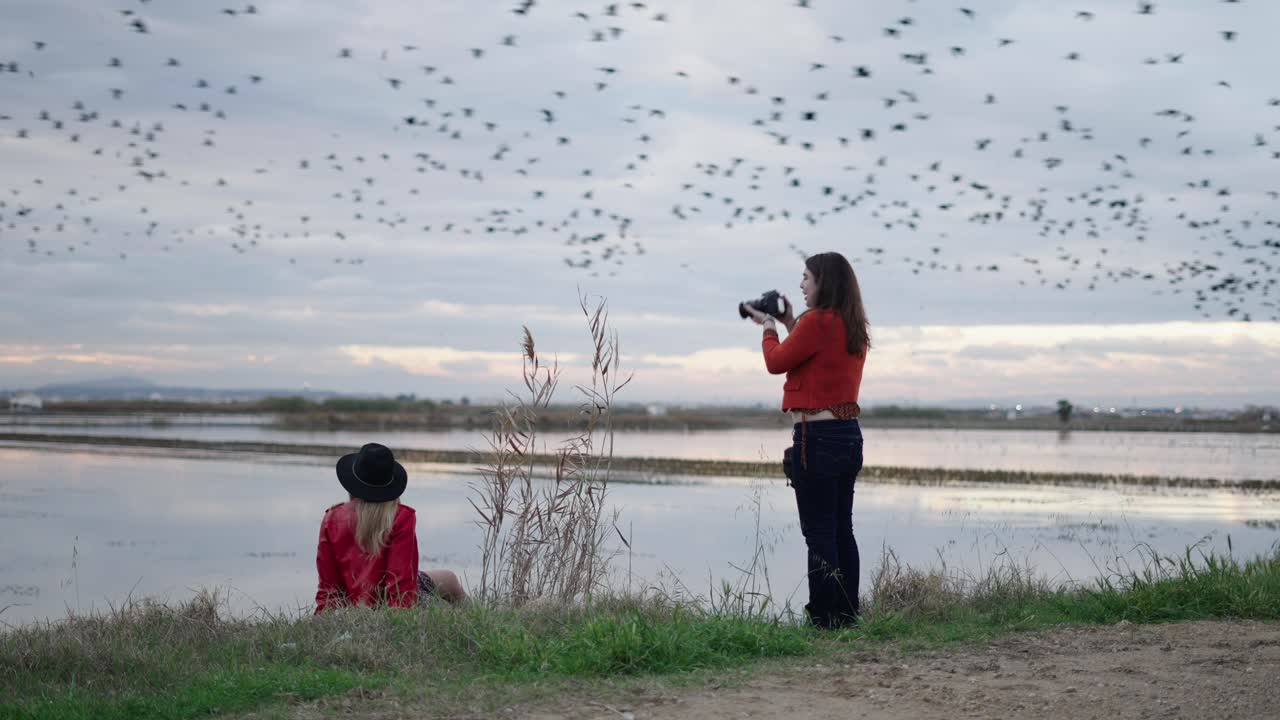 Two Women Photographing Birds in a Field at Sunset