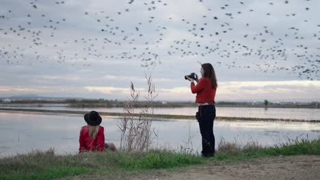 two women photographing birds in a field at sunset