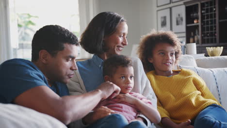 young family sitting together on the sofa in their living room watching tv and talking, close up