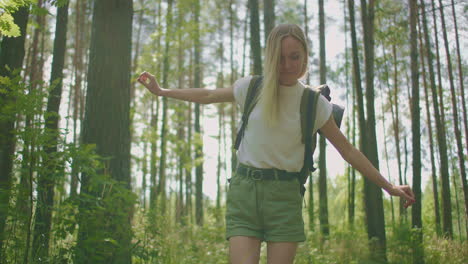 blonde woman walks through the woods with a backpack passing through a log