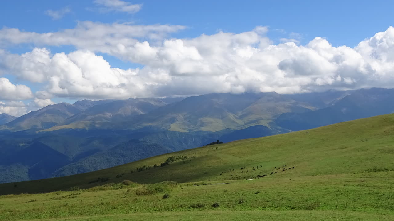 Filmato in timelapse di nuvole in rapido movimento che proiettano ombre su dolci prati alpini verdi e sulle distanti montagne del Caucaso in Russia, ampia vista paesaggistica in una giornata di sole.