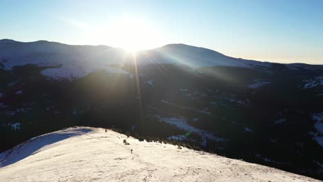 vista aérea de un excursionista caminando con raquetas de nieve en un paisaje montañoso nevado en una ruta de senderismo en montañas rocosas con el sol como contraluz